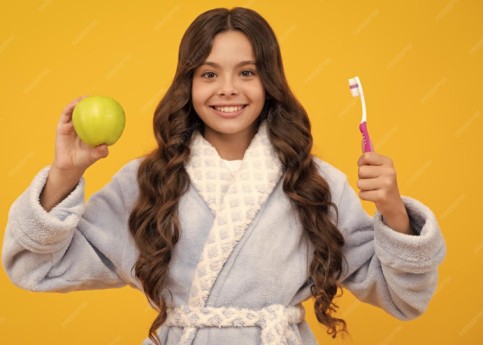 a little girl holding a toothbrush and an apple